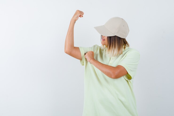 Foto grátis jovem fêmea em t-shirt, boné mostrando os músculos do braço e orgulhoso, vista frontal.