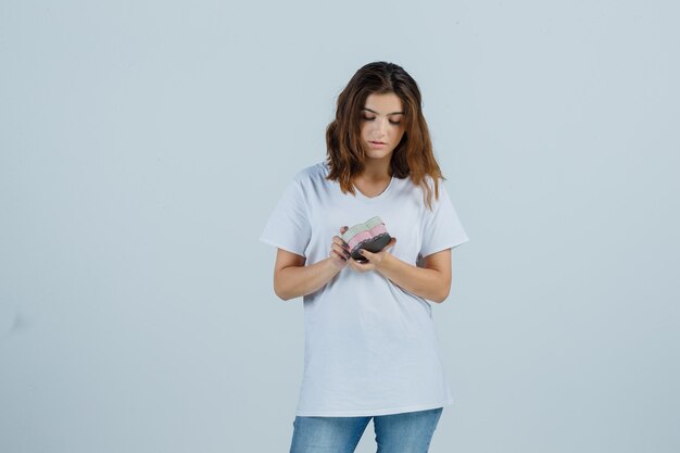 Jovem fêmea em t-shirt branca, jeans, olhando para a caixa de presente e parecendo hesitante, vista frontal.