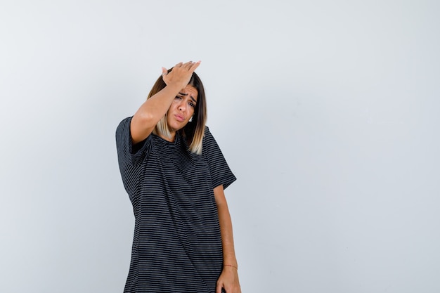 Jovem fêmea em um vestido polo, segurando a mão na cabeça e parecendo hesitante, vista frontal.