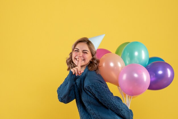 jovem fêmea escondendo balões coloridos atrás das costas em amarelo