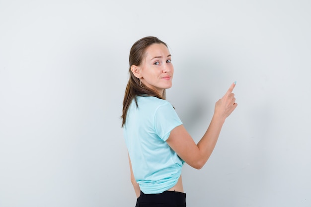 Foto grátis jovem fêmea linda apontando para o canto superior direito da camiseta e olhando feliz.