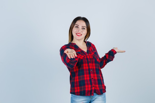 Jovem fêmea linda convidando para entrar em uma camisa casual e olhando feliz. vista frontal.