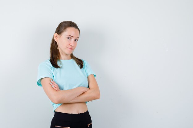 Jovem fêmea linda em t-shirt com os braços cruzados e olhando triste, vista frontal.