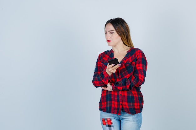 Jovem fêmea linda segurando o telefone, olhando de lado na camisa casual e olhando alegre, vista frontal.