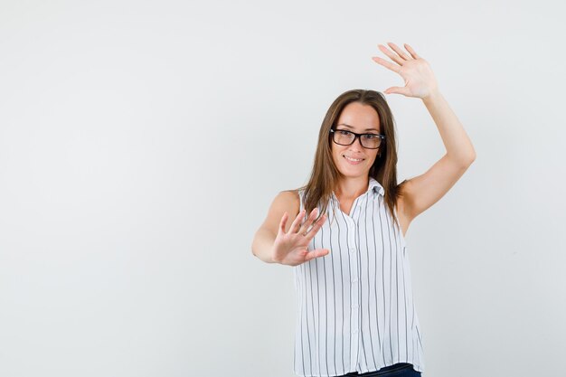 Jovem fêmea mostrando as palmas das mãos levantadas em t-shirt, jeans e olhando engraçado, vista frontal.