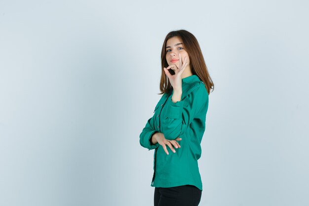 Jovem fêmea mostrando o gesto ok em camisa verde, calça e orgulhoso.