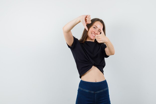 Jovem fêmea mostrando os polegares para cima e para baixo em blusa preta, calça e parecendo feliz