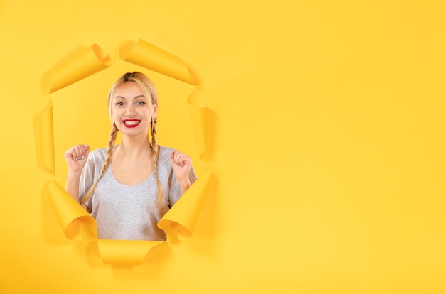 Foto grátis jovem fêmea olhando de fundo de papel amarelo rasgado venda de janela interna facial