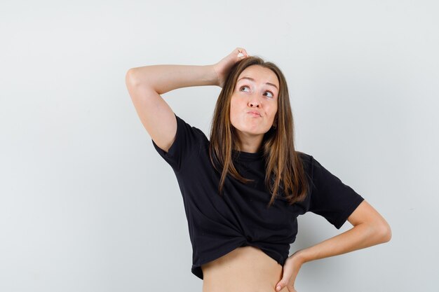 Jovem fêmea olhando para cima enquanto pensava em uma blusa preta e parecendo hesitante.