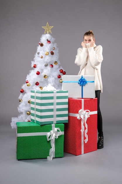 Jovem fêmea perto de presentes de natal no chão cinza