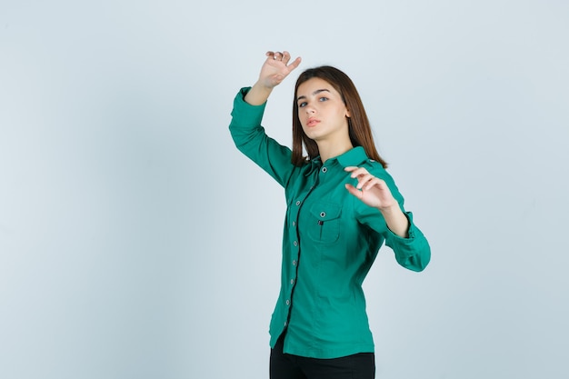 Jovem fêmea posando enquanto levanta as mãos na camisa verde e parece confiante. vista frontal.