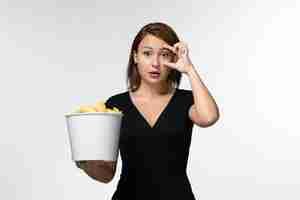 Foto grátis jovem fêmea segurando a cesta com batatas fritas e comendo na superfície branca de frente