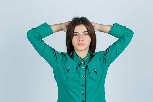 Jovem fêmea segurando as mãos atrás da cabeça em uma camisa verde e olhando orgulhosa, vista frontal.