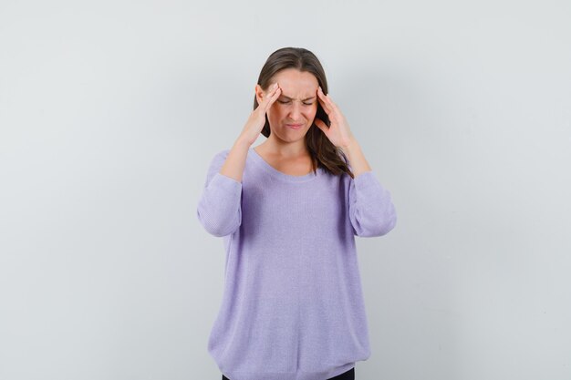 Jovem fêmea segurando as mãos na cabeça com uma blusa lilás e parecendo estressante. vista frontal.