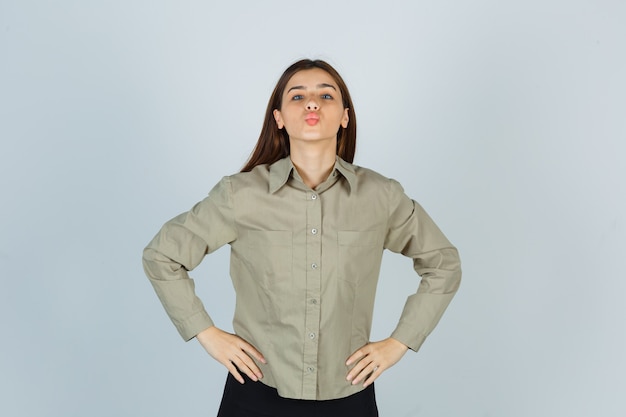 Jovem fêmea segurando as mãos na cintura, fazendo beicinho na camisa, saia e olhando bonita, vista frontal.