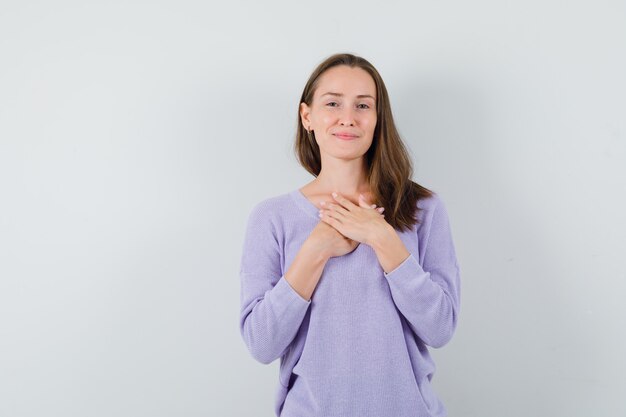 Jovem fêmea segurando as mãos no peito com uma blusa lilás e parecendo esperançosa