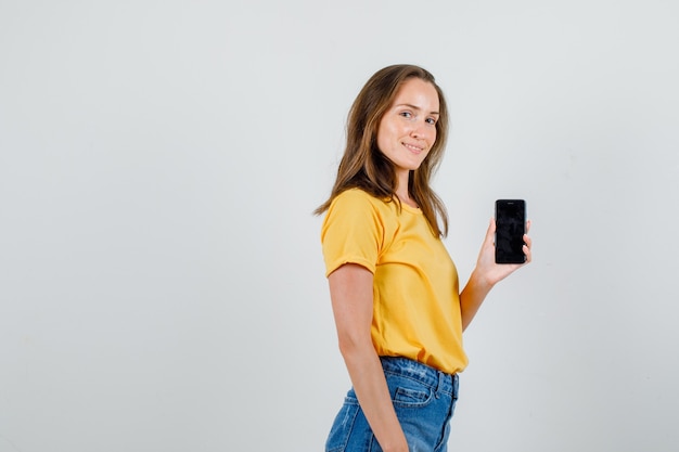 Jovem fêmea segurando o telefone móvel e sorrindo em t-shirt, shorts.