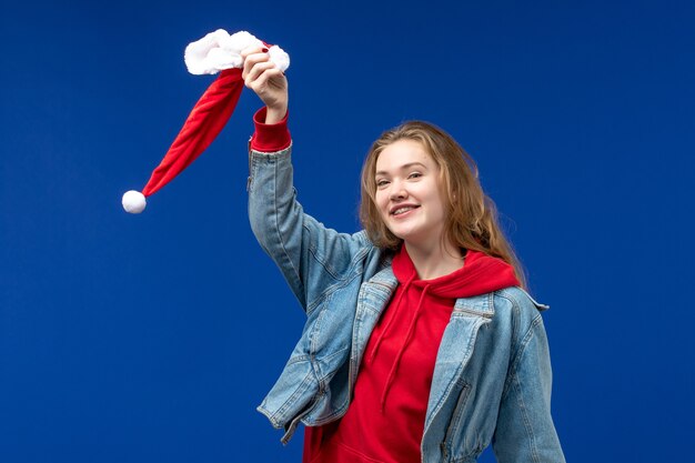 Jovem fêmea segurando um boné vermelho de natal em um fundo azul com emoções de Natal