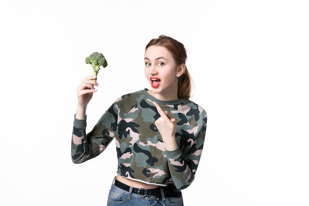 Jovem fêmea segurando um pequeno brócolis no fundo branco, vista frontal, salada, refeição, dieta, horizontal, saúde, prato