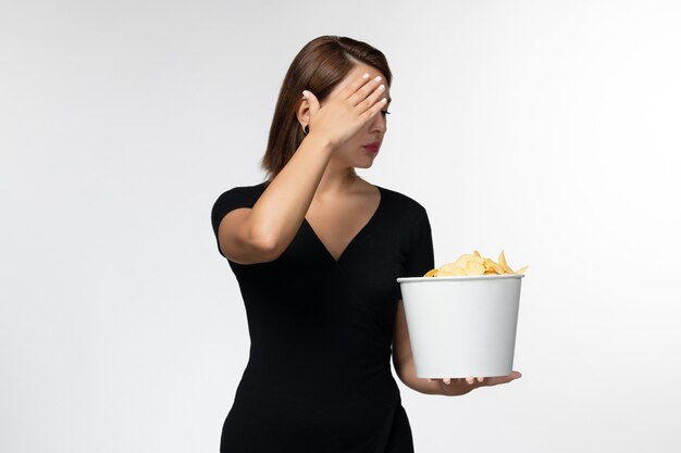 Jovem fêmea segurando uma cesta com batatas fritas de frente, assistindo a um filme em uma superfície branca.