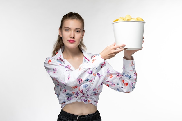 Jovem fêmea segurando uma cesta com batatas fritas de frente e assistindo filme na superfície branca