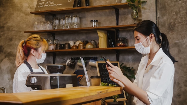 Jovem fêmea usa máscara facial de autoatendimento usar telefone celular pagar sem contato no restaurante.