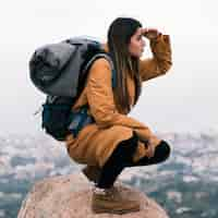 Foto grátis jovem, femininas, hiker, sentando, topo, rocha, com, dela, mochila, olho, protegendo