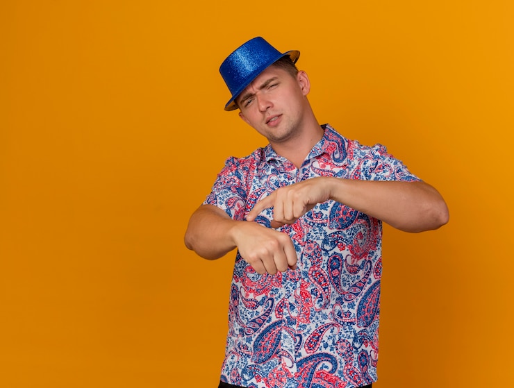 Foto grátis jovem festeiro descontente com um chapéu azul, mostrando o gesto do relógio de pulso isolado em laranja