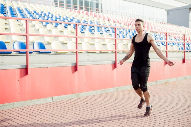 Foto grátis jovem fitness masculino pulando com corda no estádio