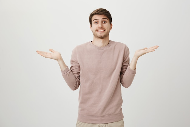 Jovem fofo sem noção dando de ombros e sorrindo sem perceber