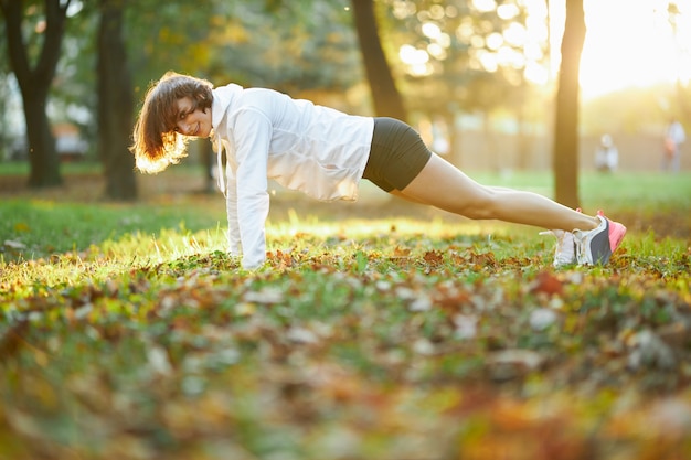 Foto grátis jovem forte fazendo exercícios de prancha em um parque ensolarado
