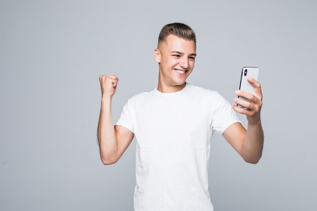 Jovem forte sorridente está vestindo uma camiseta branca e tirando uma selfie com um smartphone prata.