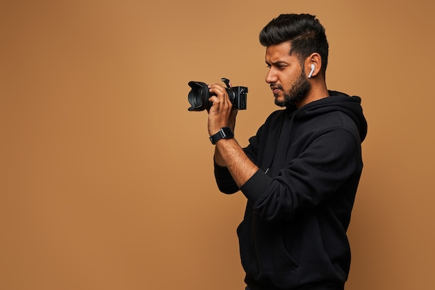 Jovem fotógrafo hindu com capuz preto e câmera na parede