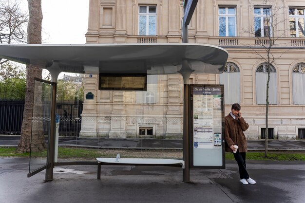 Jovem francês esperando na estação pelo ônibus e falando no smartphone