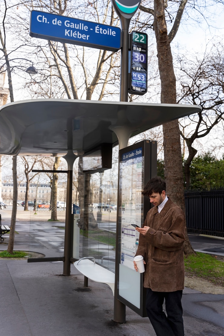 Foto grátis jovem francês esperando na estação pelo ônibus e usando seu smartphone