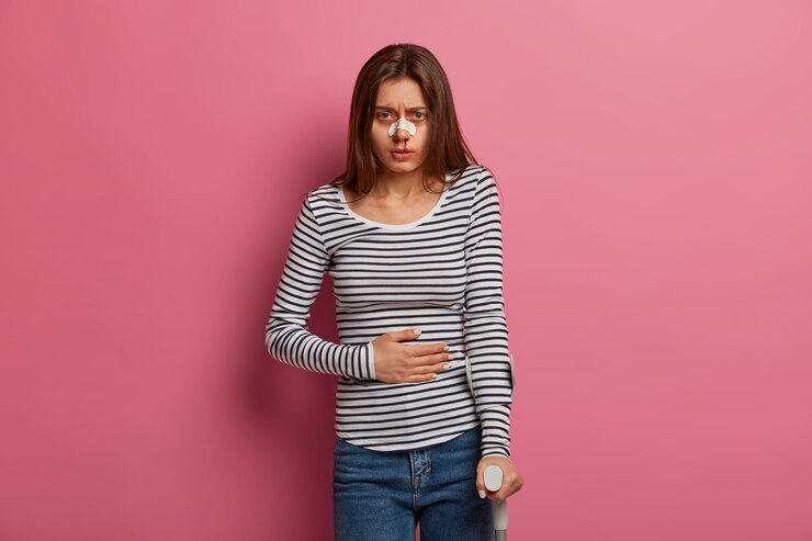 Foto grátis jovem franze a testa de dor, sente dor de estômago, tem danos físicos no corpo, passa por um programa de recuperação de reabilitação, tem sangue do nariz, isolado na parede rosa. conceito de problemas de saúde