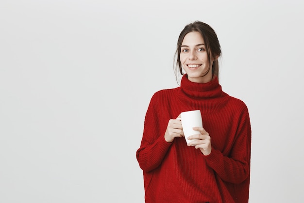 Jovem funcionária bebendo café, segurando a caneca e sorrindo