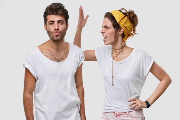 Jovem furiosa usa bandana amarela, camiseta branca casual, levanta a mão e se aproxima de algo do marido, parece negativamente, pede para não brincar de boba, tem algum mal-entendido ou discutindo