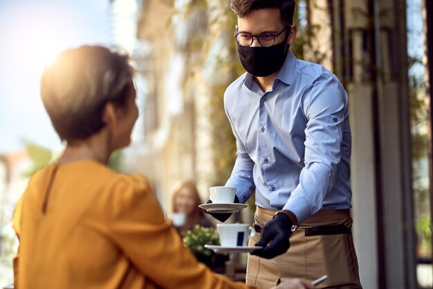 Jovem garçom usando máscara facial protetora enquanto servia café a um cliente em um café após a reabertura