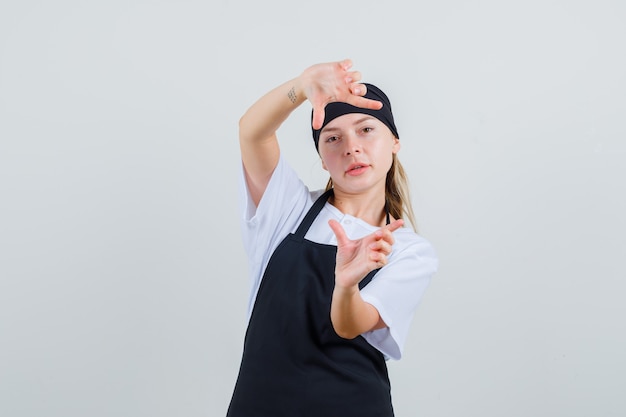 Jovem garçonete de uniforme e avental fazendo gesto de moldura