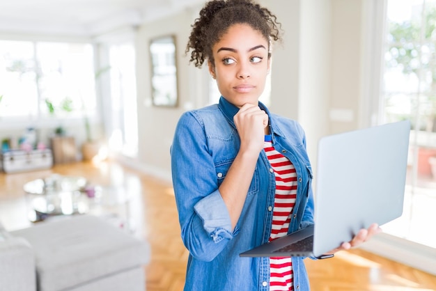 Jovem garota afro-americana de pé trabalhando usando laptop rosto sério pensando sobre a pergunta ideia muito confusa