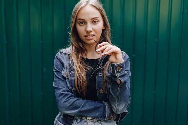 Jovem garota atraente em roupas jeans em copos em uma simples parede verde escuro com lugar para texto.