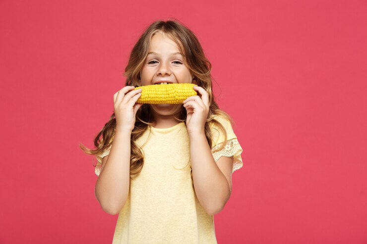 Foto grátis jovem garota bonita comendo milho sobre a parede rosa