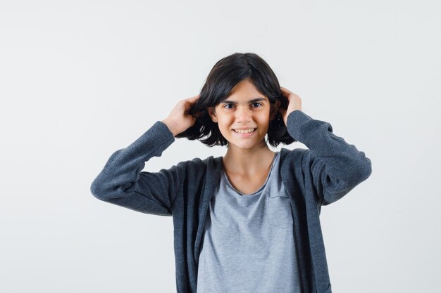 Jovem garota brincando com o cabelo em uma camiseta cinza claro e um capuz cinza escuro com zíper frontal e está linda.