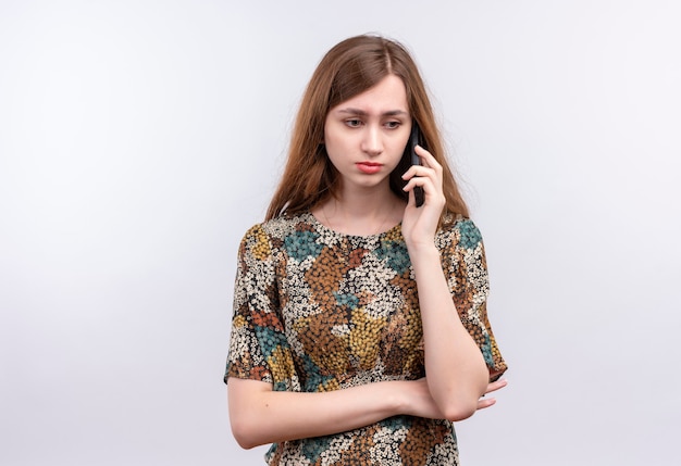 Jovem garota com cabelo comprido usando um vestido colorido franzindo a testa enquanto fala no celular