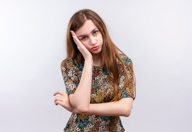 Jovem garota com cabelo comprido, usando um vestido colorido, olhando para a câmera, inclinando a cabeça por lado, cansada e entediada