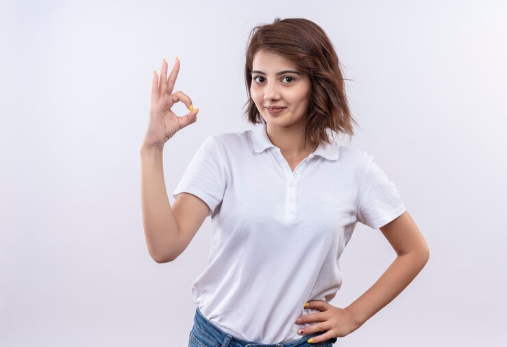 Foto grátis jovem garota com cabelo curto e camisa pólo branca sorrindo confiante fazendo sinal de ok