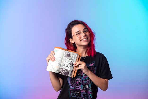 Jovem garota com cabelos rosa segurando um caderno de desenho e demonstrando-o.