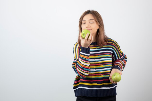 Jovem garota com roupa casual, comendo maçã verde no branco.