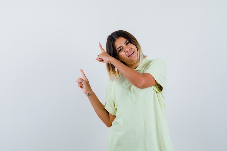 Foto grátis jovem garota em t-shirt apontando para cima com os dedos indicadores e olhando alegre, vista frontal.
